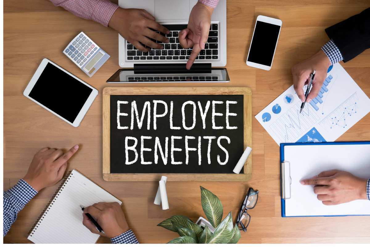 A group of coworkers sitting around a sign that reads “employee benefits” 